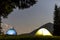 Two brightly lit tourist tents on green grassy forest clearing o