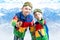 Two brothers of the boy snowboarder in bright ski jackets and goggles is skiing in the mountains.