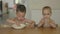 two brothers children eating together sitting at table in kitchen. elder child