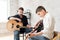 Two brothers learn to play acoustic guitar. The older brother tunes the guitar while the younger one runs his finger