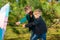 Two brothers are pulling a colored umbrella against the wind in a pine forest