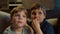 Two brothers watching TV, eating popcorn sitting on couch at home. Two boys watching exciting movie at home. Siblings on