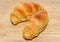 Two brown baked croissants, wooden plate, close up