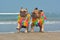Two brown French Bulldog dogs wearing matching colorful tropical hawaiian flower garland while running at beach