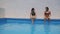 Two brown girls in bikinis laugh and elbow each other in the pool