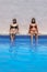 Two brunette girls sitting on the edge of the pool while they sunbathe