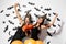 Two brunette women in black dresses and witches hats have fun with jack-o-lanterns on a white background with bats and