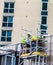 Two builders in retro-reflective clothing and helmets on scaffolding are engaged in repair work