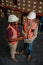 Two business man wearing hardhats doing research for processing deliveries holding digital tablet standing in warehouse