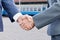 Two businessman are shaking their hands at the overhead railway background. The concept is the interaction of different business