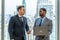 Two Businessman using a laptop together while standing in front of office building windows overlooking the city, Boss discuss