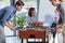 Two businessmen playing table football while young businesswomen chatting during break