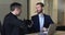 Two businessmen sit at desk shake hands, finish formal meeting