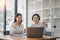 Two businesswomen show joyful expression of success at work smiling happily with a laptop computer