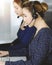 Two busineswomen have conversations with the clients by headsets, while sitting at the desk in a sunny modern office