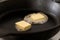 Two butter pats melting on a black cast iron frying pan.