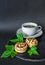 Two cake biscuits with cream, banana and chocolate and a cup of coffee on a slate dish on a black background, decorated with green