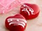 two cakes in the form of glazed red hearts on a pink marble table, close-up