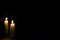 Two candles on dark background. Lighting candles on black. Yellow wax candle with warm flame.