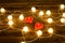 Two candles shape of heart among the glowing lanterns made of rattan on a wooden background.