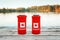 Two cans of beer in red cozy beer can cooler with Canadian flag standing on wooden pier by lake outdoors. Friends celebrating