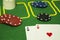 Two cards - a black clubs ace and a red hearts ace - with diverse colored chips at a green poker table