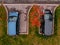 Two cars blue and black parked in interesting place among green grass strewn with yellow autumn leaves.