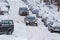 Two cars drive through a snowy yard between rows of parked cars in deep snow in Tula, Russia.