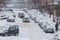 Two cars drive through a snowy yard between rows of parked cars in deep snow in Tula, Russia.