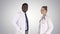 Two caucasian and Afro American smiling doctors standing looking in to camera on gradient background.