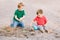 Two Caucasian children sitting in sandbox playing with beach toys. Little boys friends having fun together on playground. Summer