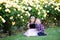 Two Caucasian kids sitting on a green grass in a rose garden and hugging, brother and sister, siblings,