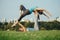 Two Caucasian women doing yoga stretching workout in park outdoors at sunset