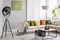 Two ceramic vases standing on modern coffee table in bright living room with elegant corner sofa, industrial lamp and golden lime