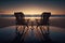 Two chairs on the beach at sunset with reflection in water