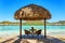 Two chairs and coffee table under a thatched parasol on a sand b