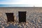 Two chairs next to each other in the sand by the sea. seascape, blurred walking people in the background
