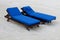 Two chaise loungers on a sandy beach.