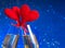 Two champagne flutes with golden bubbles and red velvet hearts make cheers on blue bokeh background