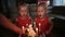 Two charming twin sisters in beautiful red dresses are waiting for a cake with burning candles. They blow candles and