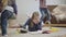 Two cheerful Caucasian children running around elder sister lying on soft carpet and reading. Teen girl trying to