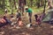 Two cheerful couples of young hikers are getting ready for a meal, lady cooks, guy is fixing the fire, other couple chilling, sit