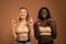 Two cheerful cute teenage international girls standing isolated over orange background, holding fingers crossed for good