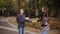 Two cheerful friends ride and dance on an electronic scooter in an autumn park.