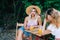 Two cheerful friends sitting on a pier lake, on summer day, communicate and drink lemonade