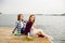 Two cheerful happy skater girl in hipster outfit having sitting on a wooden pier during summer vacation