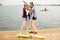 Two cheerful happy skater girls in hipster outfit having fun on a wooden pier during summer vacation