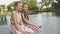 Two cheerful little girls sit on a wooden bridge on the banks of the river, laugh and swing their legs on a summer