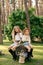 Two cheerful preteen girls sitting on stump among tall trees in summer forest