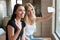 Two cheerful women indoors using mobile phone and waving